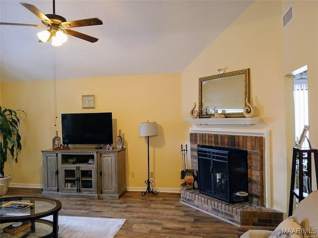 living room featuring ceiling fan, vaulted ceiling, a brick fireplace, and dark wood-type flooring