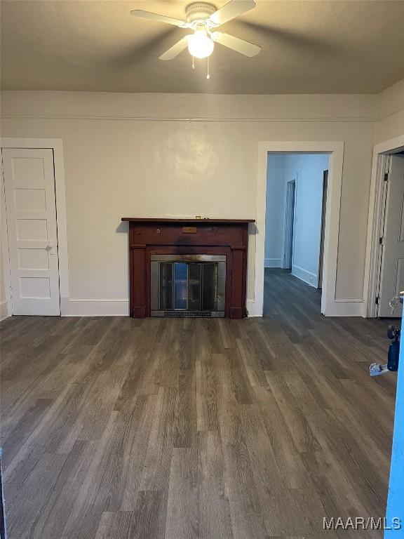 unfurnished living room featuring dark wood-style floors, ceiling fan, a glass covered fireplace, and baseboards