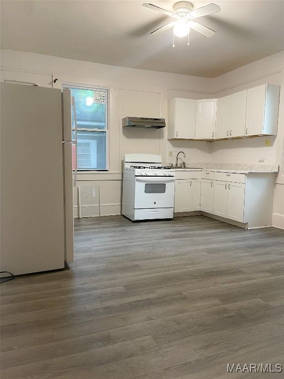 kitchen featuring under cabinet range hood, white appliances, white cabinetry, light countertops, and dark wood-style floors