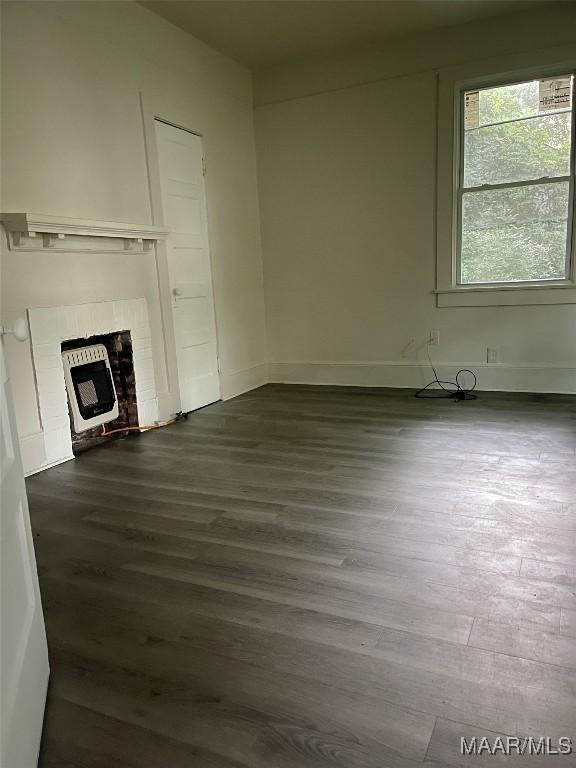 unfurnished living room with dark wood finished floors, baseboards, a fireplace, and heating unit