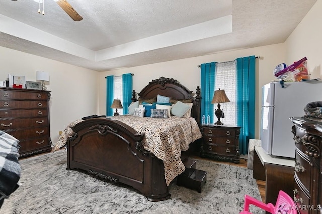 bedroom featuring a textured ceiling, ceiling fan, a raised ceiling, and white fridge