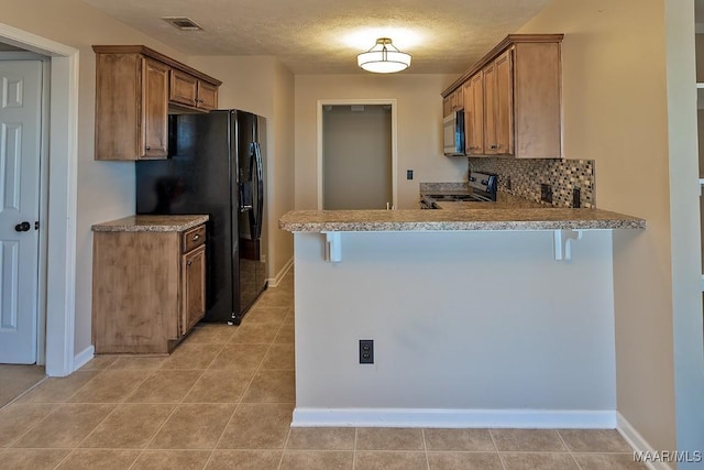 kitchen featuring kitchen peninsula, decorative backsplash, a kitchen breakfast bar, stainless steel appliances, and a textured ceiling