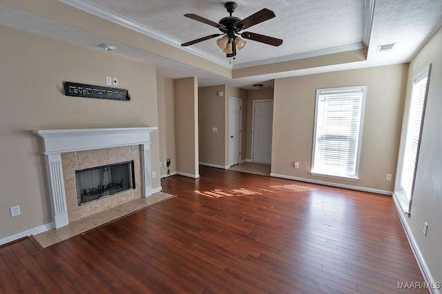 unfurnished living room with a fireplace, dark hardwood / wood-style floors, ornamental molding, ceiling fan, and a tray ceiling