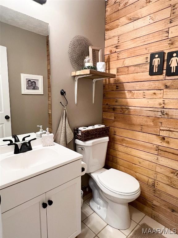 bathroom featuring toilet, tile patterned flooring, wooden walls, and vanity