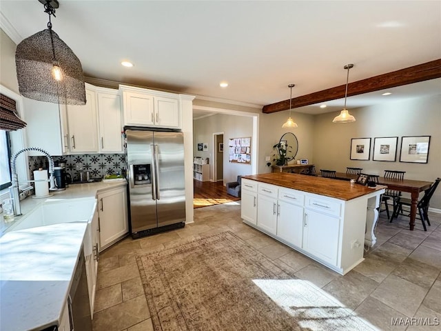 kitchen featuring white cabinets, butcher block counters, beamed ceiling, hanging light fixtures, and stainless steel fridge