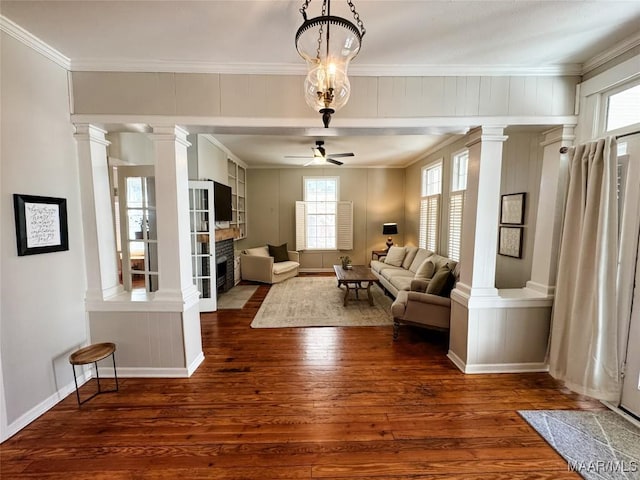 unfurnished room with dark hardwood / wood-style flooring, crown molding, ceiling fan with notable chandelier, and a stone fireplace