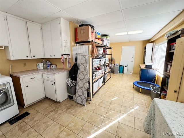 kitchen with light tile patterned floors, a paneled ceiling, washer / dryer, and white cabinetry