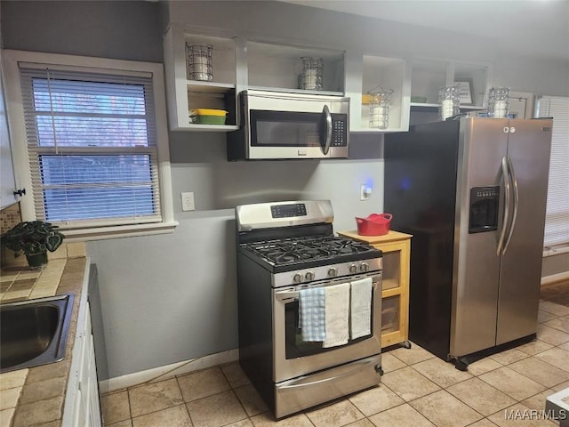 kitchen with light tile patterned floors, sink, tile countertops, and stainless steel appliances