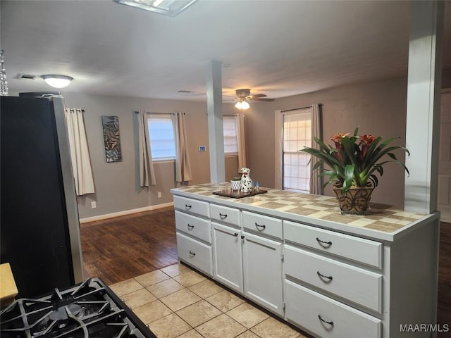 kitchen with white cabinetry, tile countertops, ceiling fan, light tile patterned flooring, and stainless steel refrigerator