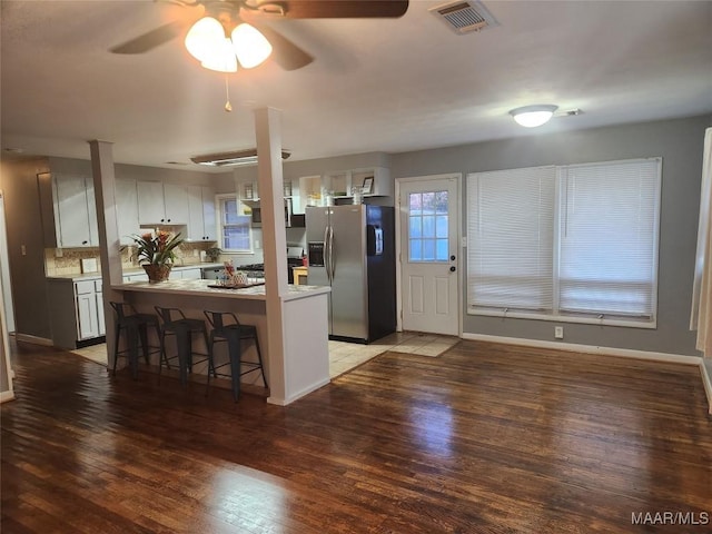 kitchen with stainless steel fridge, ceiling fan, a kitchen breakfast bar, dark hardwood / wood-style flooring, and white cabinets