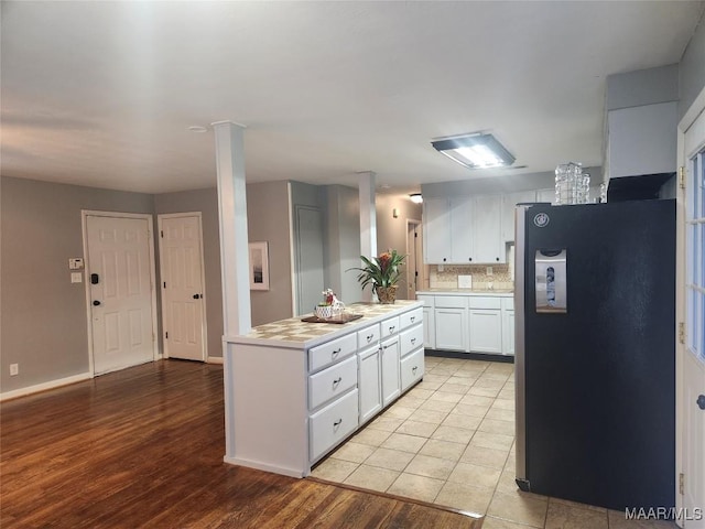 kitchen with ornate columns, light tile patterned floors, backsplash, stainless steel refrigerator, and white cabinets