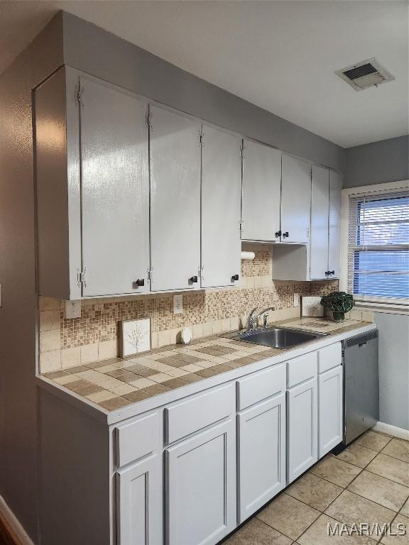 kitchen featuring stainless steel dishwasher, white cabinets, backsplash, and sink