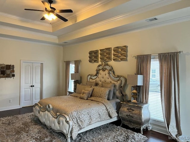 bedroom with ceiling fan, dark hardwood / wood-style floors, a tray ceiling, ornamental molding, and a closet