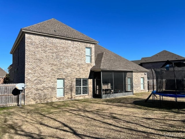 rear view of property with a trampoline, a sunroom, and a lawn