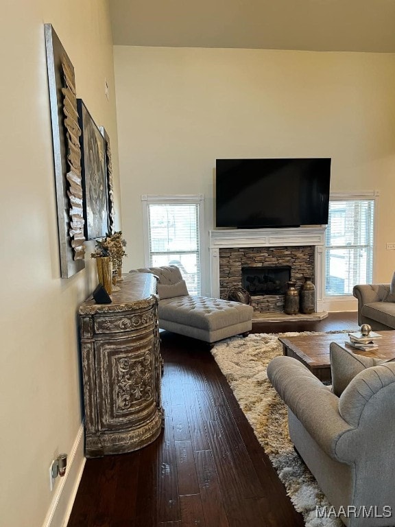 living room featuring dark wood-type flooring, a healthy amount of sunlight, and a stone fireplace