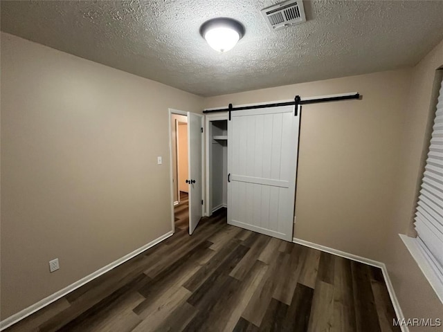 unfurnished bedroom with dark wood-type flooring, a closet, a barn door, and a textured ceiling