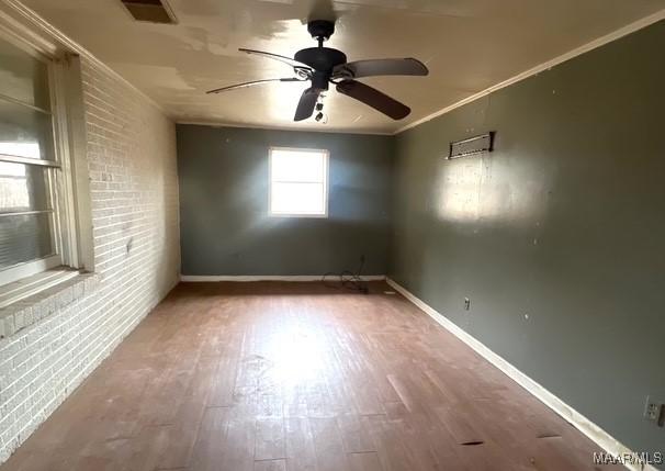 unfurnished room with ceiling fan, brick wall, crown molding, and wood-type flooring