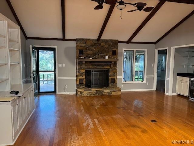 unfurnished living room featuring ceiling fan, wood-type flooring, lofted ceiling with beams, and a stone fireplace