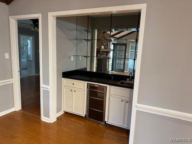 bar with dark wood-type flooring, sink, white cabinets, and beverage cooler