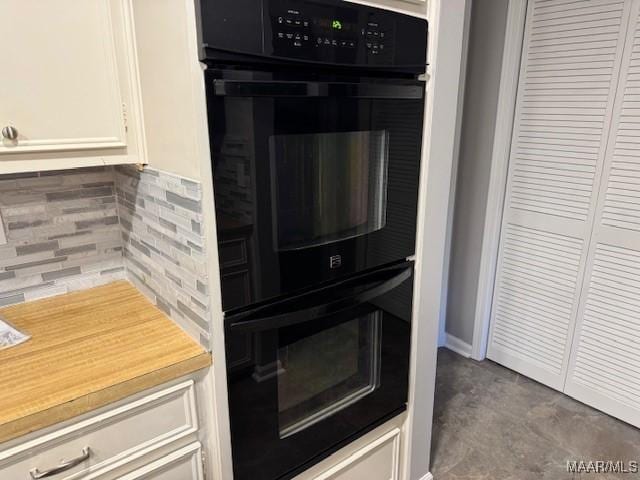 kitchen with backsplash, black double oven, and white cabinetry