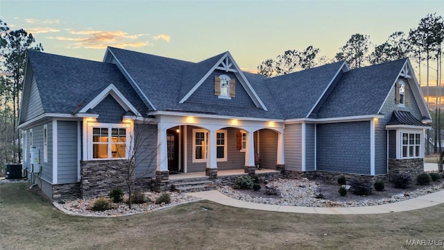 craftsman-style house with stone siding, a porch, central AC, and roof with shingles