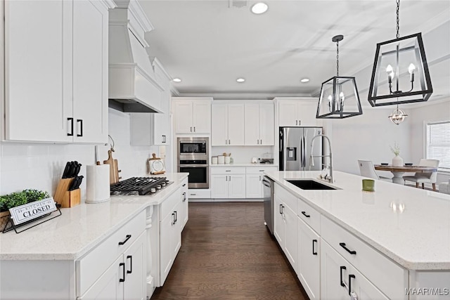 kitchen with stainless steel appliances, a sink, white cabinets, a center island with sink, and crown molding