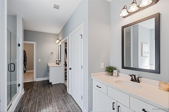 bathroom with a shower stall, visible vents, two vanities, and a sink