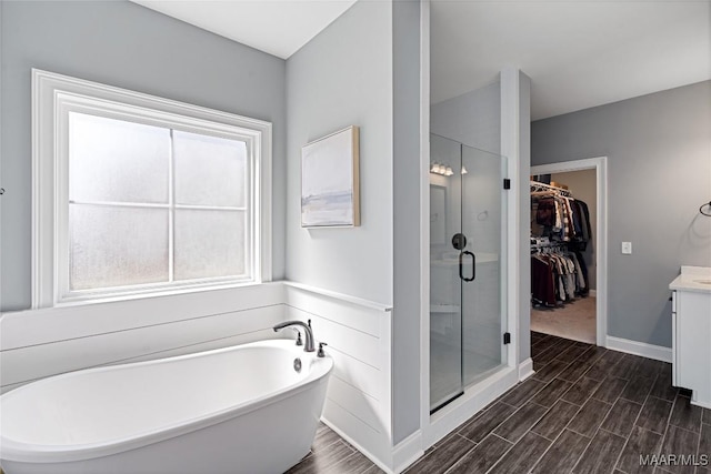 full bath featuring a stall shower, wood tiled floor, a walk in closet, vanity, and a freestanding tub