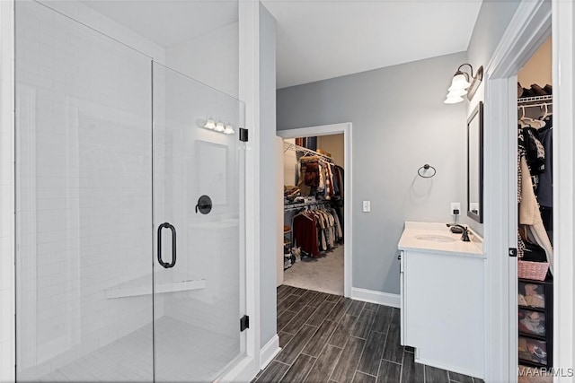 bathroom featuring a spacious closet, a stall shower, wood tiled floor, vanity, and baseboards