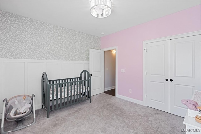 bedroom featuring carpet floors, a closet, wainscoting, a nursery area, and wallpapered walls