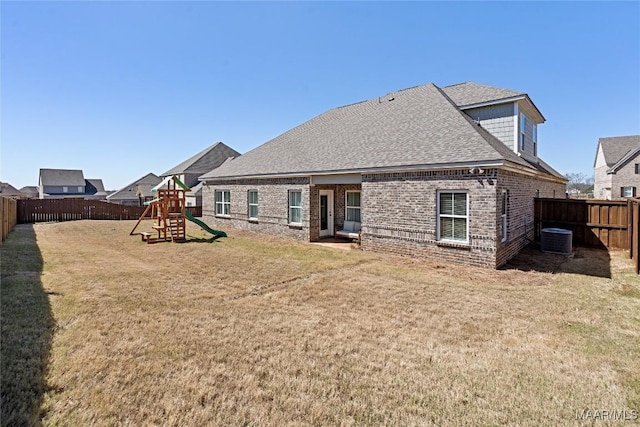 back of house with a playground, a yard, brick siding, a shingled roof, and a fenced backyard