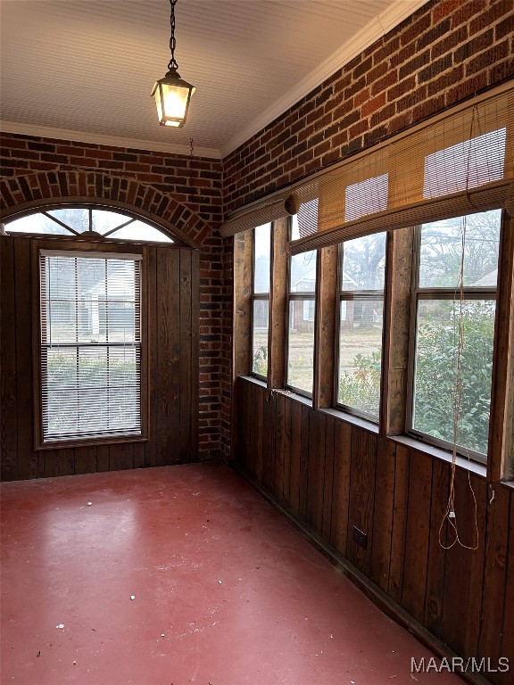 spare room featuring crown molding, brick wall, plenty of natural light, and concrete floors