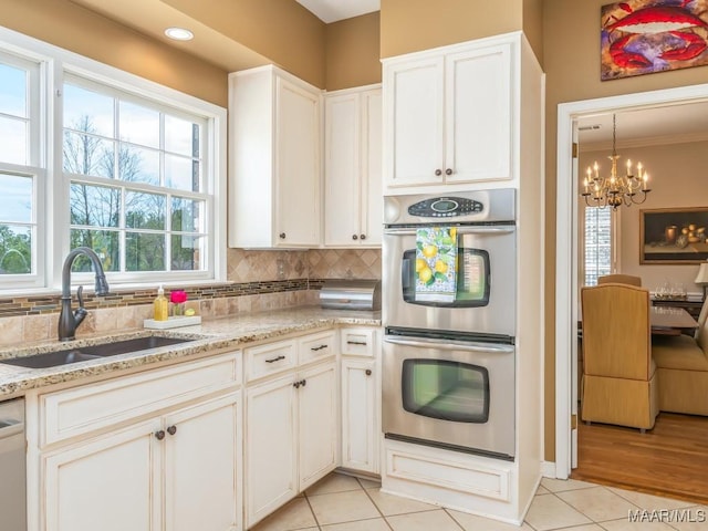 kitchen featuring light stone counters, sink, double oven, and light tile patterned flooring