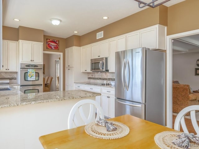 kitchen with light stone counters, white cabinetry, decorative backsplash, and appliances with stainless steel finishes