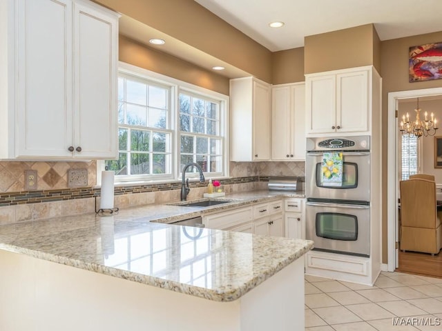 kitchen with kitchen peninsula, sink, white cabinetry, and stainless steel double oven