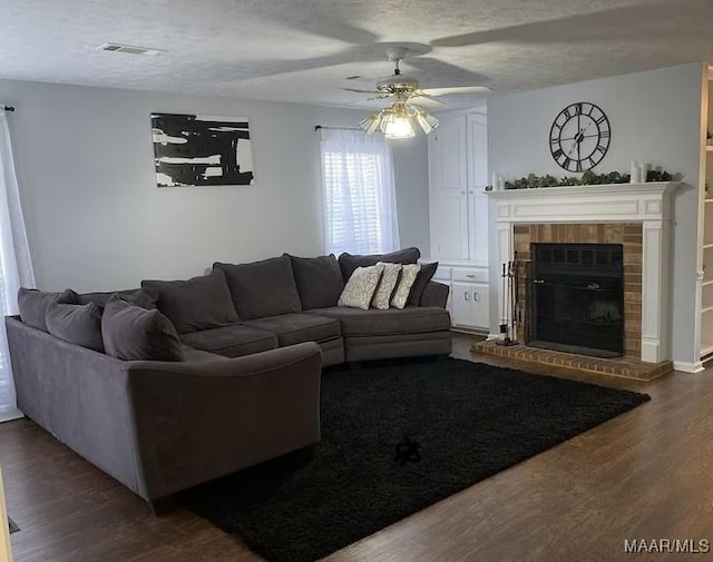 living room with ceiling fan, hardwood / wood-style flooring, a textured ceiling, and a brick fireplace