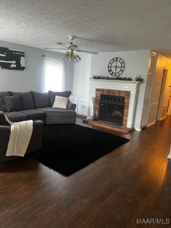 living room with ceiling fan, a textured ceiling, a brick fireplace, and dark hardwood / wood-style flooring