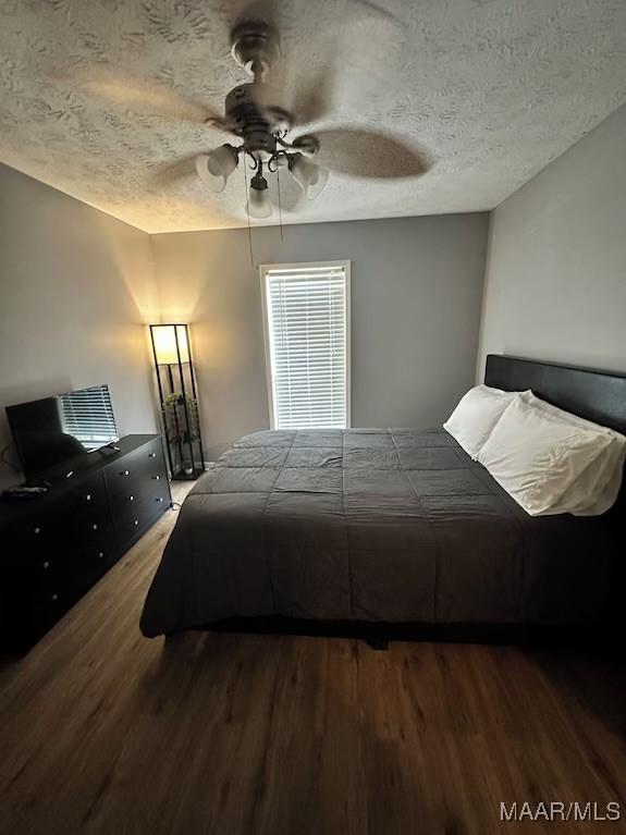 bedroom with ceiling fan, hardwood / wood-style floors, and a textured ceiling