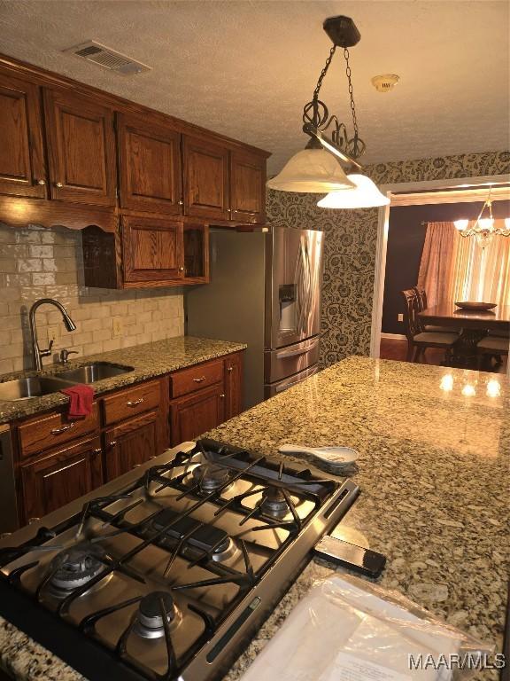 kitchen with stainless steel refrigerator with ice dispenser, tasteful backsplash, sink, hanging light fixtures, and gas range oven