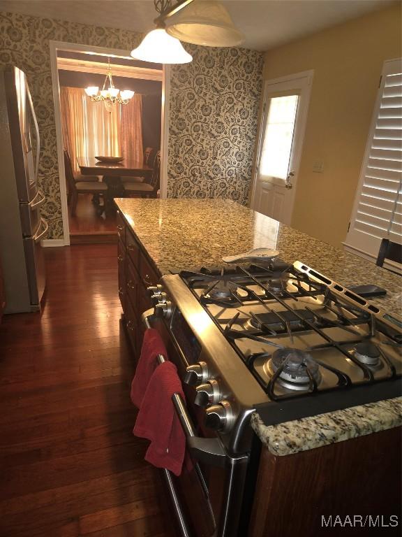 kitchen featuring light stone countertops, a chandelier, pendant lighting, dark hardwood / wood-style flooring, and stainless steel appliances