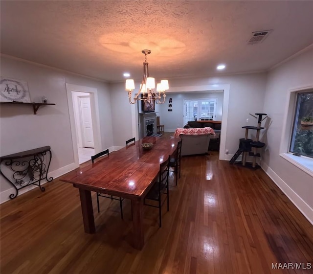 dining space featuring dark wood-type flooring, crown molding, a textured ceiling, and a notable chandelier