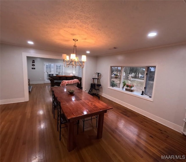 dining area with dark wood-type flooring, ornamental molding, a chandelier, and a textured ceiling