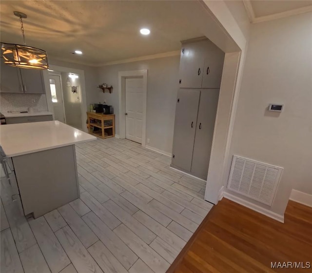 kitchen featuring pendant lighting, crown molding, light hardwood / wood-style flooring, gray cabinetry, and a kitchen island