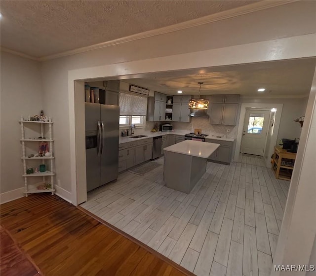 kitchen with sink, light hardwood / wood-style flooring, appliances with stainless steel finishes, a center island, and decorative light fixtures