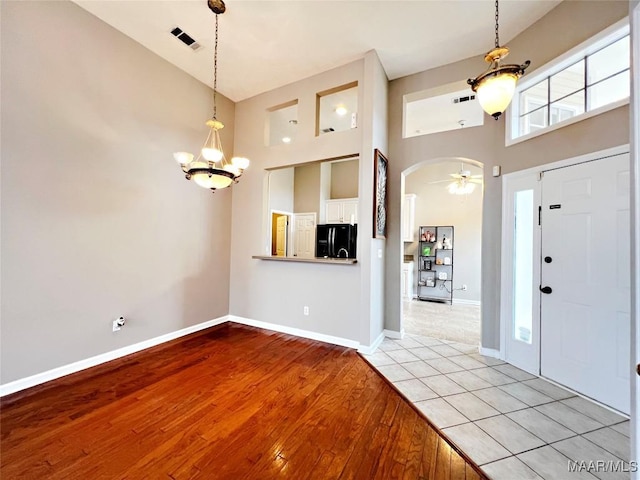 tiled entryway featuring ceiling fan with notable chandelier and a high ceiling