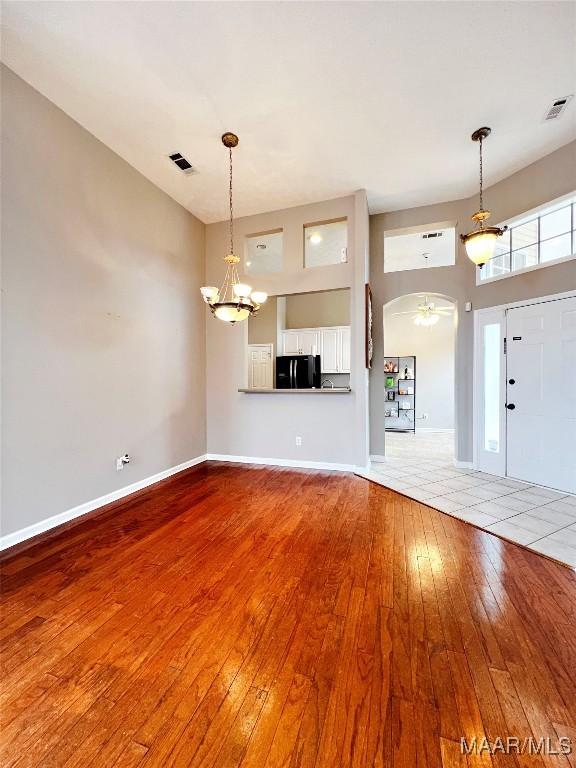 unfurnished living room with a towering ceiling, a notable chandelier, and light wood-type flooring