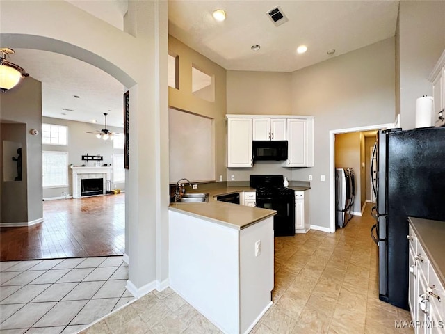 kitchen with black appliances, washing machine and clothes dryer, white cabinetry, light tile patterned floors, and sink