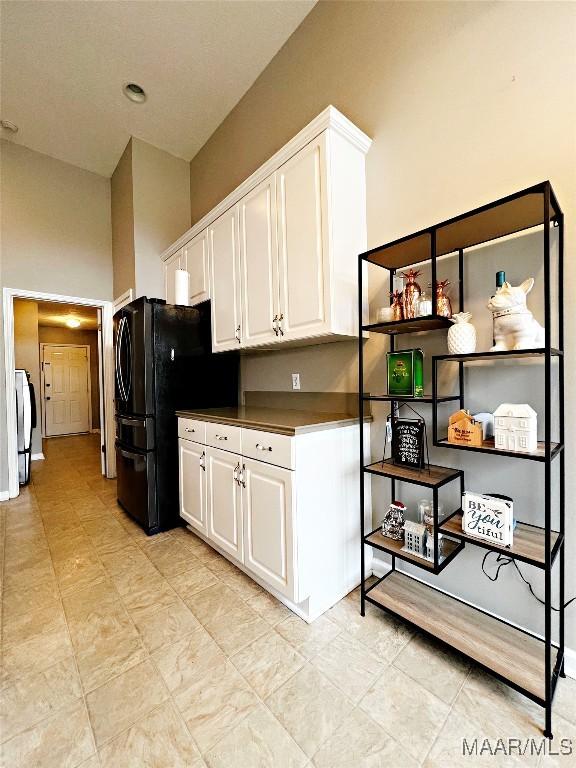 kitchen featuring black fridge, white cabinetry, and washing machine and clothes dryer