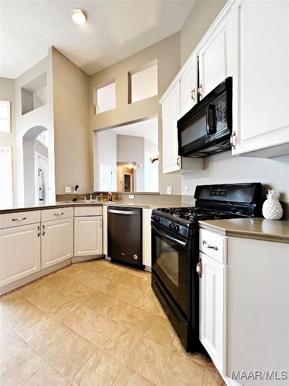 kitchen with black appliances, a towering ceiling, and white cabinets