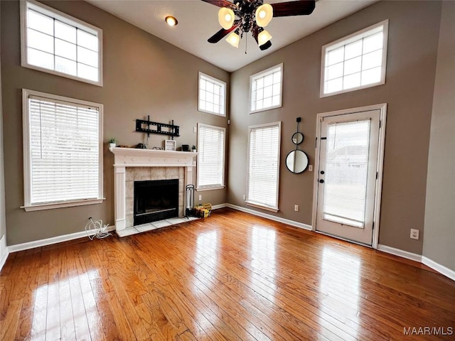 unfurnished living room with ceiling fan, a towering ceiling, light hardwood / wood-style flooring, and a tiled fireplace